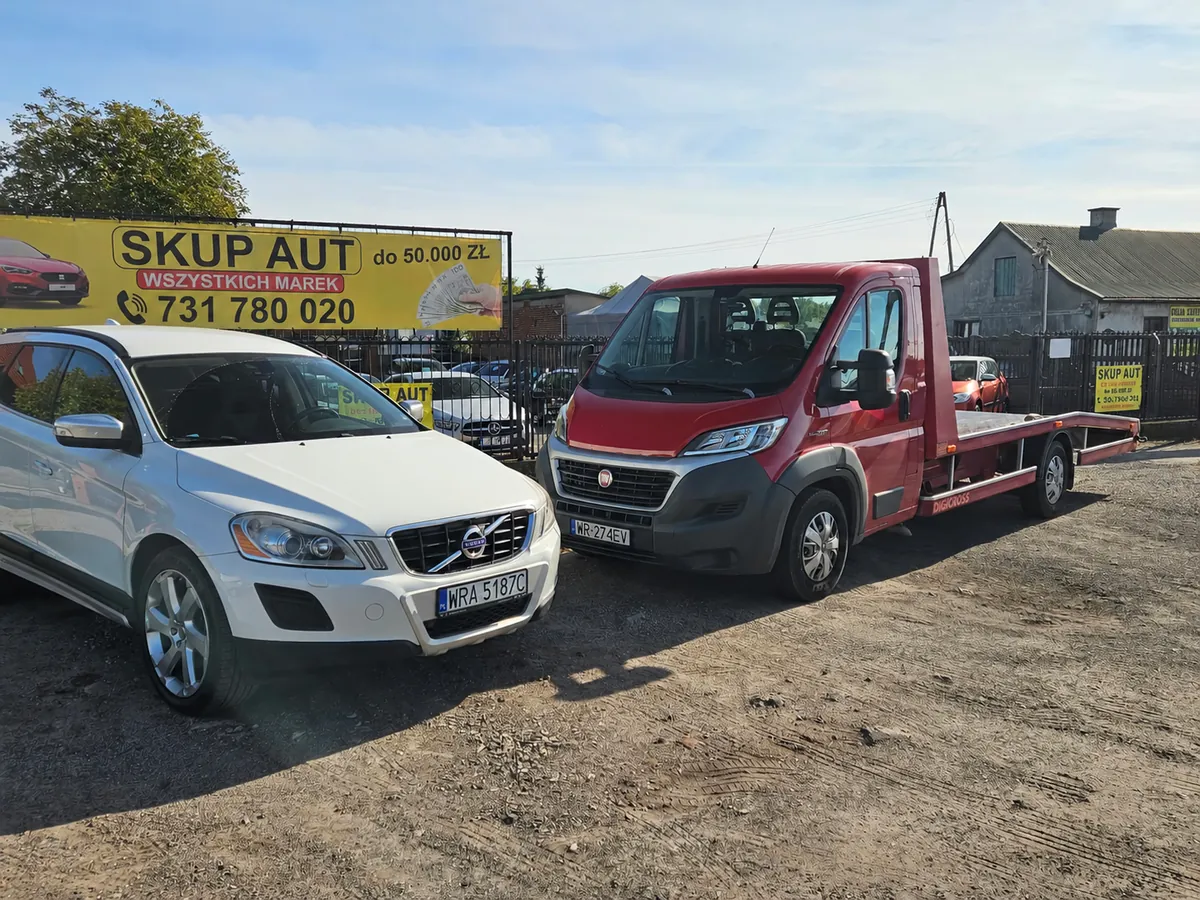 Czerwona laweta Skup Aut Kielce obok białego Volvo, w tle billboard z numerem 731 780 020